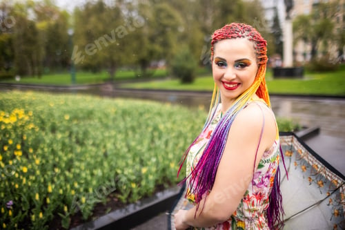 Preview: A beautiful girl with bright multi-colored braids and an elegant umbrella walks in a spring park in