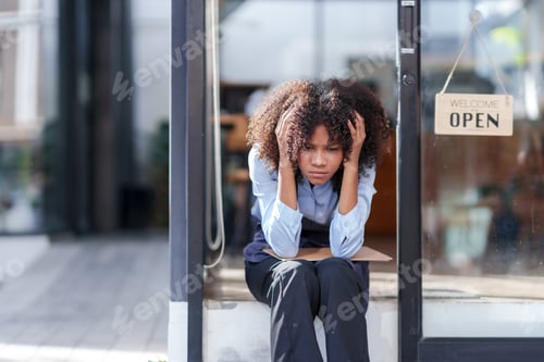 Preview: Female shopkeeper sitting stressed out at the store entrance frustrated by the economic impact.