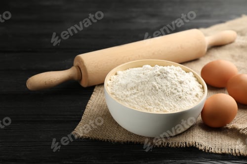 Preview: Bowl of flour, eggs and rolling pin on black wooden table