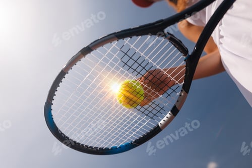 Preview: Close-up of tennis racket and ball against blue sky, dynamic sports shot with sunlight effect