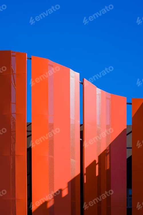 Preview: Orange curved steel wall decoration outside of building against blue clear sky in vertical frame
