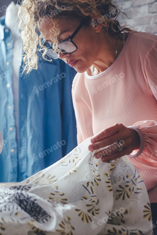 Preview: Mature dressmaker woman sews clothes on sewing machine. Concentrated seamstress