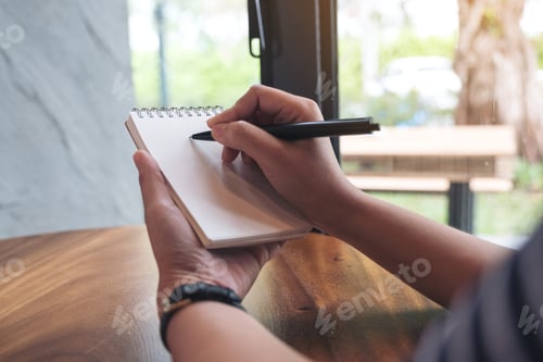 Preview: Closeup image of a woman's hands writing down on a white blank notebook