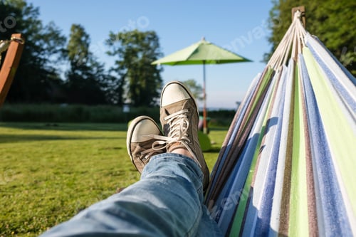 Preview: Feet in sneakers and jeans in a hammock, camping, against the backdrop of a summer landscape.