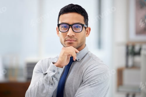 Preview: Young serious mixed race businessman standing alone in an office at work. Face of a confident hispa