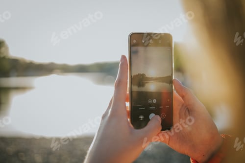 Preview: Person taking pictures of the sunset over the lake with the phone