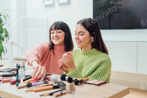 Preview: Young ethnic women sitting at table and applying lipstick and makeup in room