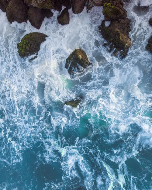 Preview: Vertical overhead aerial shot of a wavy blue sea against the rocks