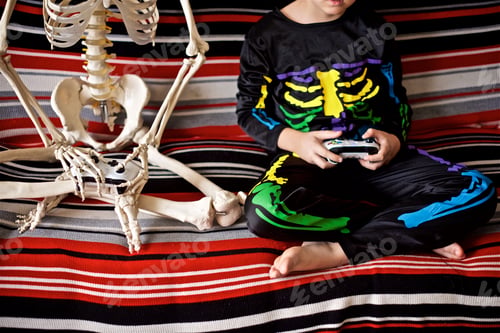 Preview: Young boy dressed as a coloured skeleton play video game with skeleton