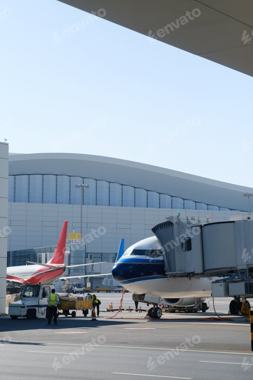 Preview: Airplanes at busy airport terminal with boarding bridge connecting to plane under clear blue sky