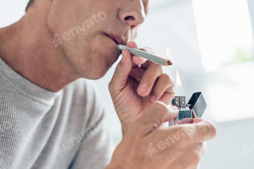Preview: cropped view of man lighting up blunt with medical cannabis