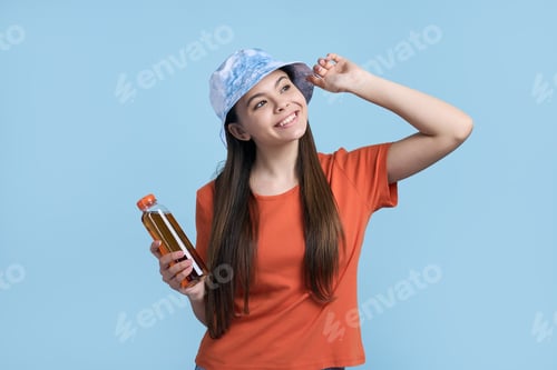 Preview: Happy teen girl in orange t-shirt and stylish blue panama hat, holds a bottle with refreshing drink