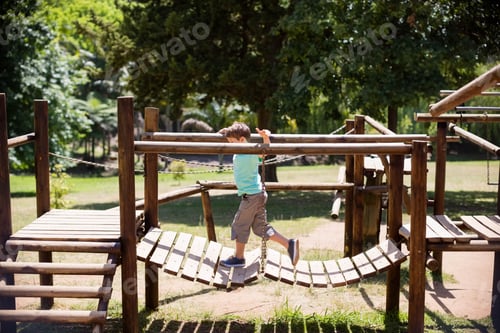 Preview: Suspended wooden plank bridge swinging over grassy ground near dirt pathways in sunny park
