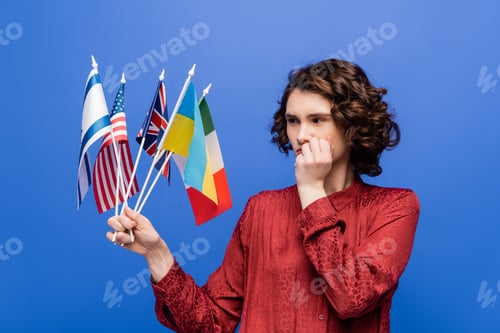Preview: thoughtful woman holding hand near face while looking at flags of different countries isolated on