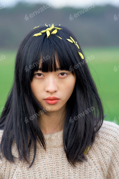 Preview: Woman with long black hair and yellow petals on head stands in a field. Brandenburg, Germany