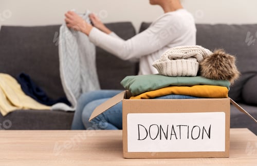 Preview: Female Volunteer preparing used clothes for donation in a cardboard box at home