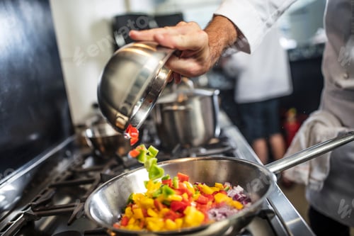 Preview: Chef pouring sliced vegetables into pan on stove, close-up