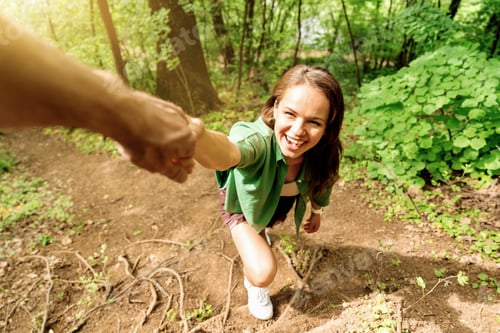 Preview: Smiling woman climbing forest trail holding man's hand, hiking together on sunny day.