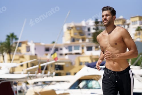 Preview: Young man with an athletic body running shirtless through a harbour