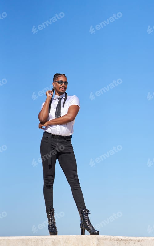 Preview: Stylish androgynous man posing against blue sky