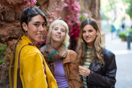 Preview: Smiling young women walking together in an urban setting with flowers - stylish friendship outdoor