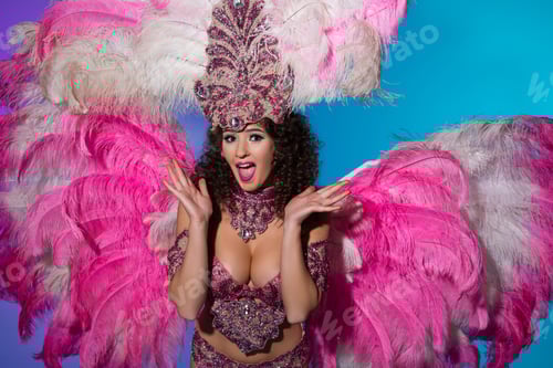 Preview: Surprised young woman in carnival costume with pink feathers isolated on blue background