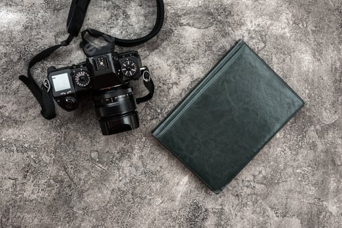 Preview: photocamera and a notebook lying on a plaster background