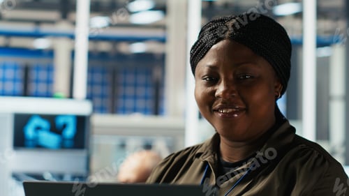 Preview: Portrait of smiling engineer in factory uses laptop to check parameters