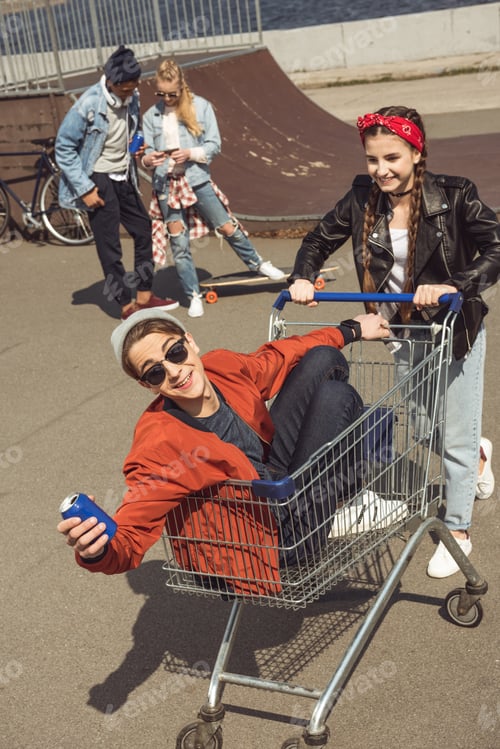 Preview: teenagers having fun with shopping cart in skateboard park, hipster style concept