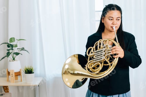 Preview: Dressed in black, a woman blows a gleaming French horn in gold