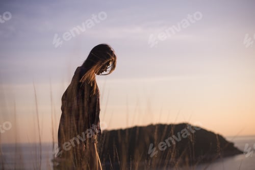 Preview: Hipster stylish woman traveler looking on a sea or ocean at the sunset