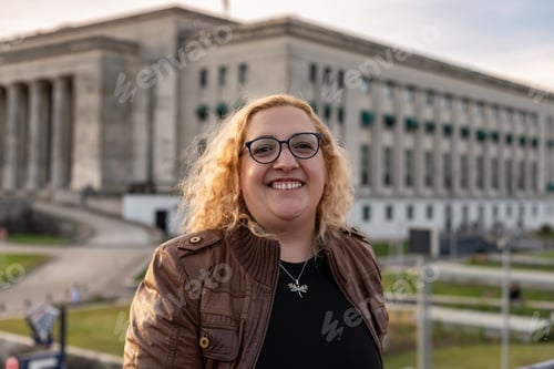 Preview: Portrait of a blonde and curly plus-size woman looking at camera while smiling in a University backg