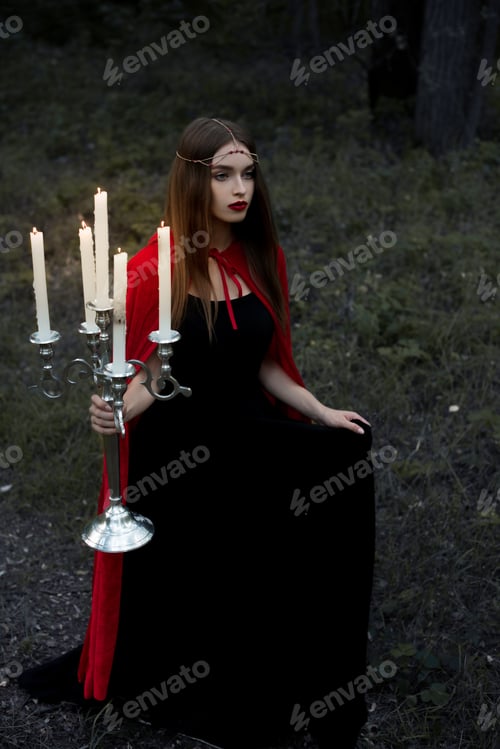 Preview: mystic girl in red cloak holding candelabrum with flaming candles walking in forest