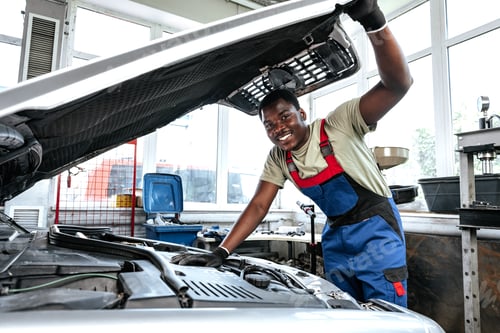 Preview: Young African man working under the hood of car fixing engine in auto service