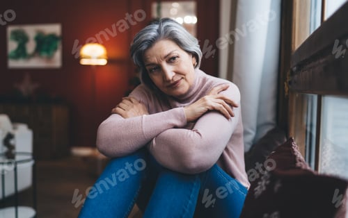 Preview: Thoughtful mature woman sitting on couch with folded hands