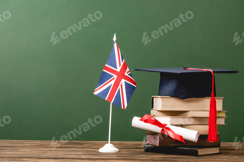 Preview: Books, academic cap, diploma and british flag on wooden surface isolated on green