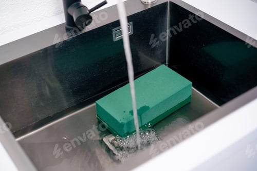 Preview: close up In a flower shop florist soaks green foam in an iron sink to form flower arrangements