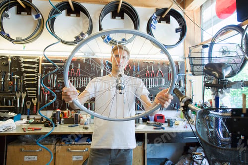 Preview: Mid adult man in repair shop looking through bicycle wheel
