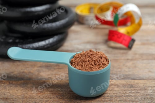 Preview: Scoop with protein powder, measuring tape and dumbbell plates on wooden table. Space for text