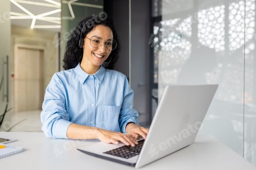 Preview: Young beautiful woman with video call headset working inside office at workplace, Hispanic online