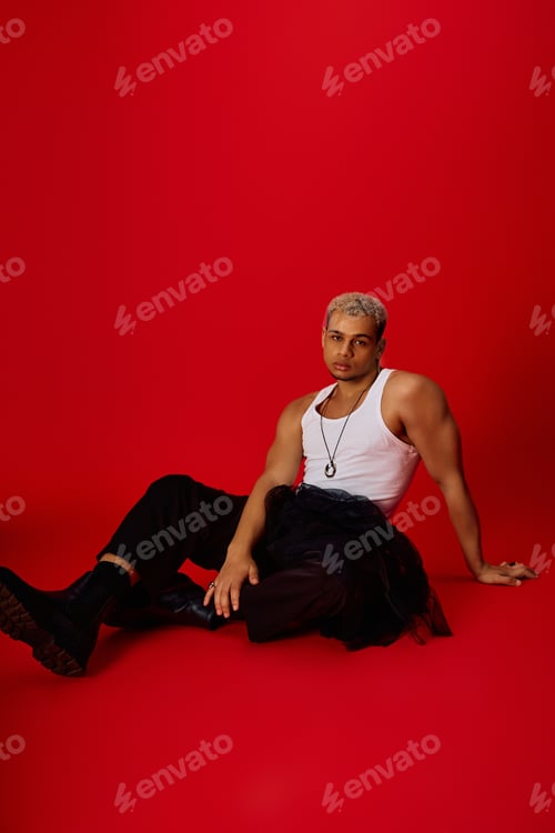 Preview: Young man in trendy attire showcasing style in vibrant red studio