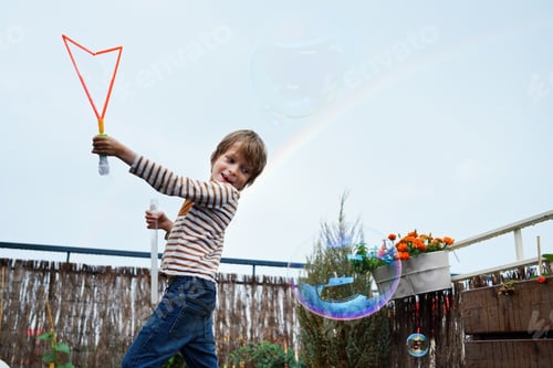 Preview: The International Blowing Bubbles Day. Happy boy making bubbles on roof terrace in rainy sunny day