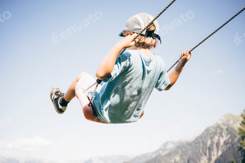 Preview: Rear view of boy wearing baseball cap on playground swing, Bludenz, Vorarlberg, Austria
