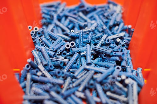 Preview: Plastic blue dowels on red background, wall plugs for fixation and installation, close up, top view