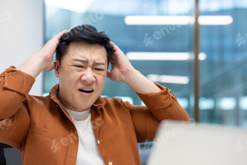 Preview: Frustrated Asian businessman holding head in office, experiencing stress and anxiety at work