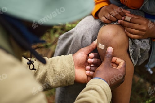 Preview: Middle Aged Black Man Applying Bandage to Knee of Black Boy Outdoors