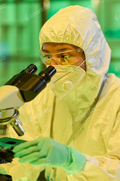 Preview: Serious young female biochemist looking in microscope in scientific laboratory