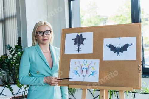 Preview: Psychologist in eyeglasses pointing at Rorschach test on board in consultation room