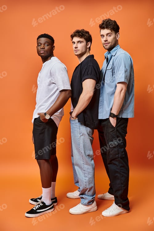 Preview: attractive elegant diverse friends in urban attires posing on orange backdrop, fashion concept