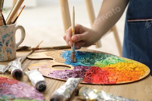Preview: Woman with paintbrush mixing paints on palette at wooden table indoors, closeup